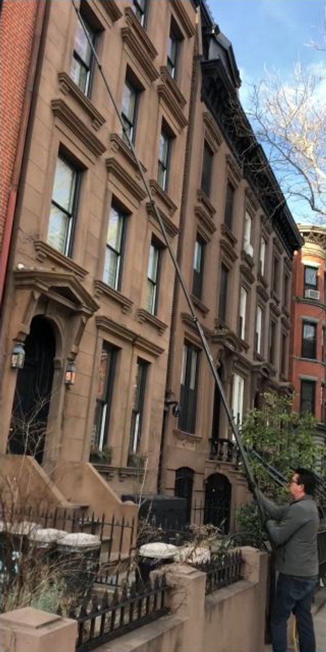 Owner using a water-fed pole to clean windows on a Brooklyn brownstone